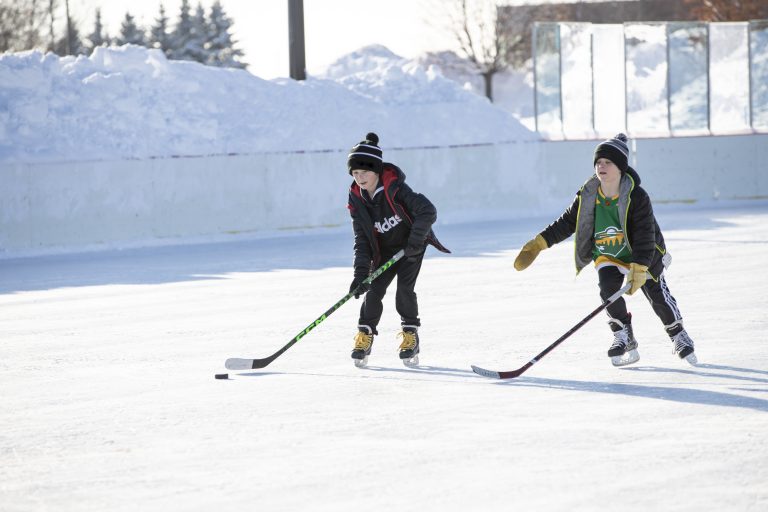 Two boys playing hockey on an outdoor rink