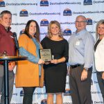 A group of people smiling while holding one award