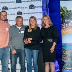 A group of people smiling as women in middle holds award
