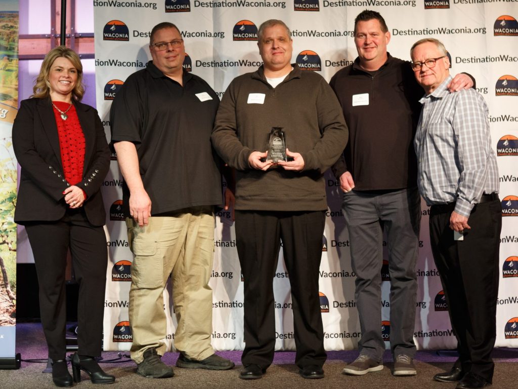 Five people posing with one person holding an award trophy