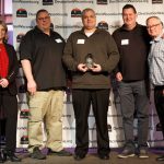 Five people posing with one person holding an award trophy