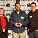 Three people posing with award winner holding award