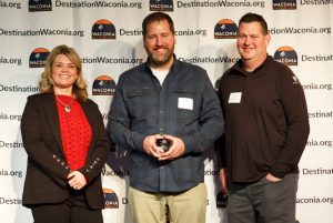 Three people posing with award winner holding award