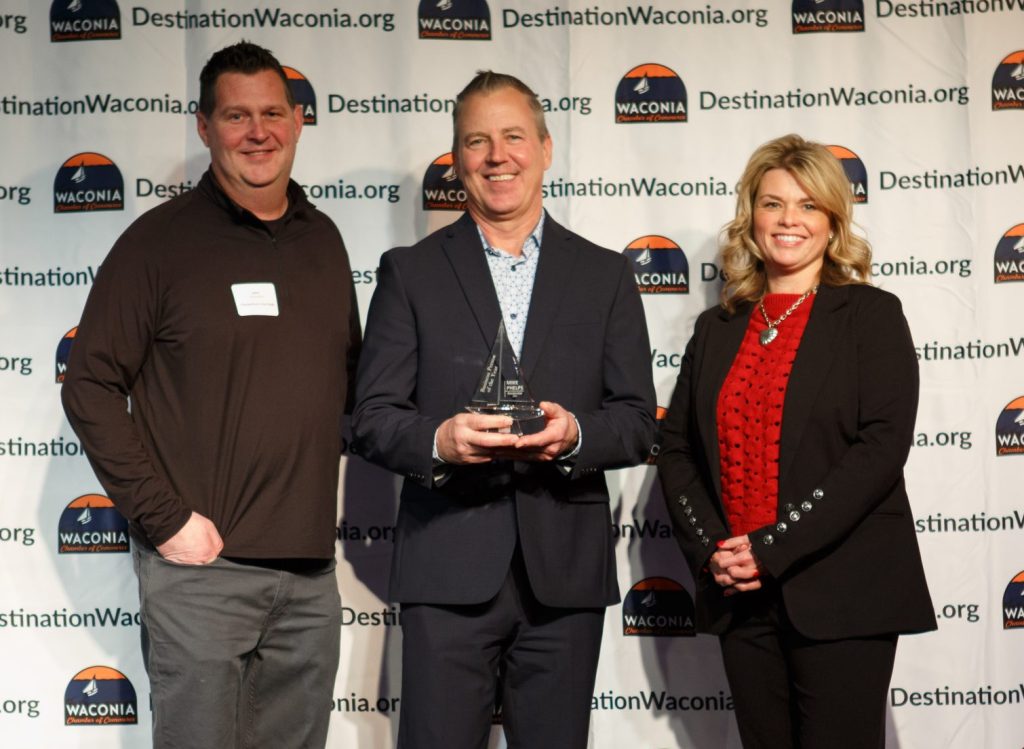 Three people posing with middle person holding award trophy