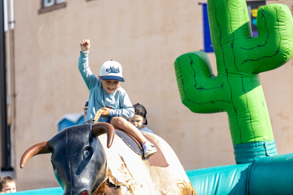 A boy smiling and riding on a mechanical bull
