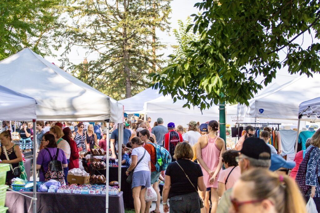 A crowd shopping in the park lined with arts and crafts vendors