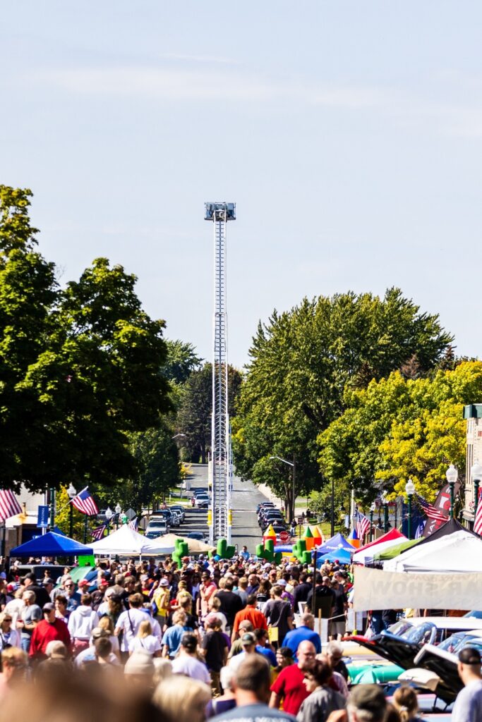 A crowd of people walking on the street with a firetruck ladder extended in the background